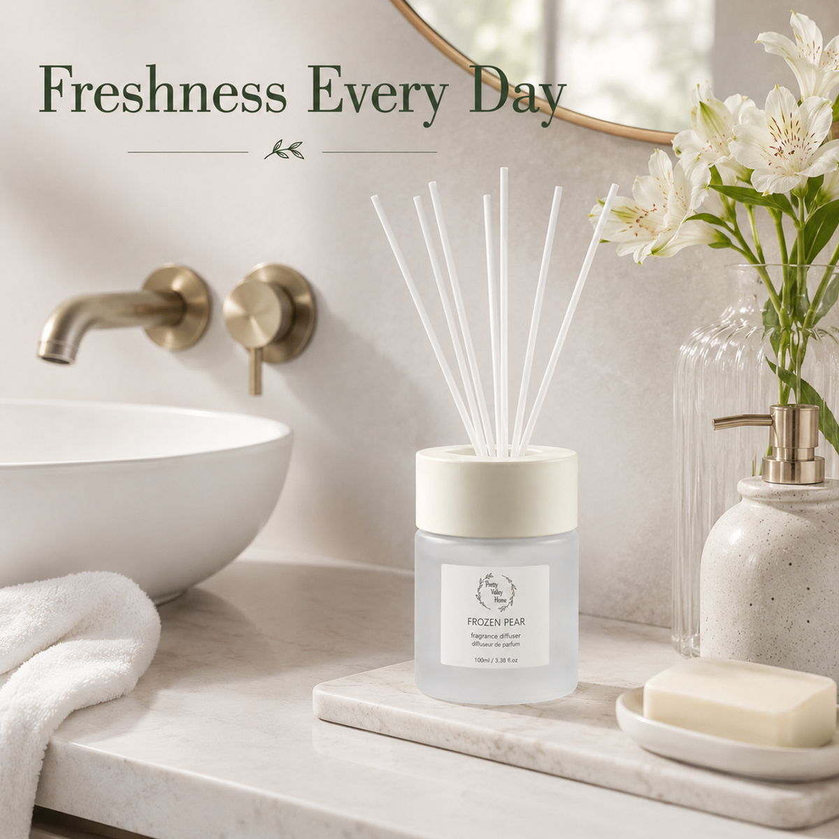 A frosted glass reed diffuser bottle with a cream lid and white reeds, placed on a marble tray in a bathroom setting. The scene includes a white sink, brass faucet controls, a vase of white flowers, a soap dish with a bar of soap, and the text 'Freshness Every Day' at the top.