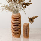 Two honeycomb-patterned wooden vases in different heights, filled with dried grasses and botanicals, set on a light marble surface against a plain off-white background.