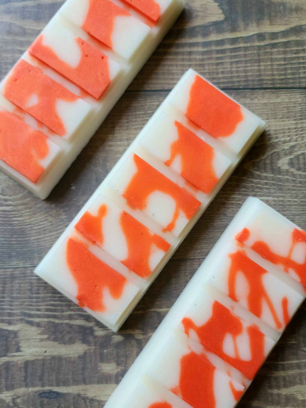 Three unwrapped Pumpkin Spice Latte soy wax melt snap bars, white wax with orange swirls, on a wooden surface.