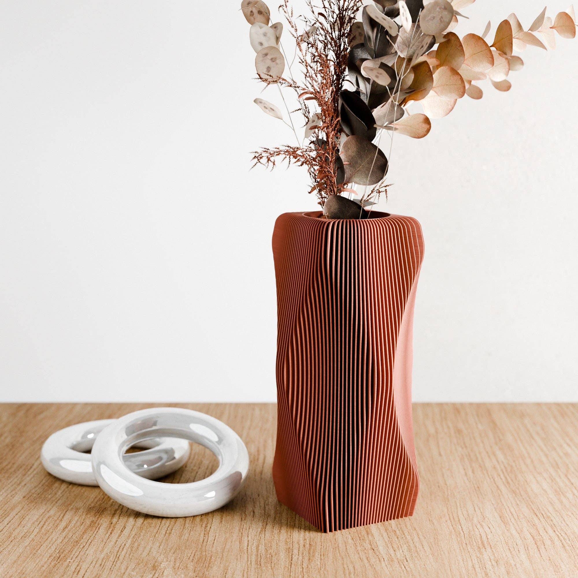 Decorative vase with wavy design and dried plants on a wooden surface
