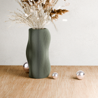 Green textured vase with dried plants on a wooden surface