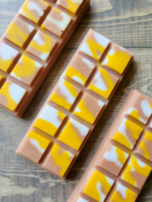 Three unwrapped Caramel Frappe soy wax melt snap bars, caramel-brown wax with yellow and white swirls, on a wooden surface.