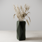 Black textured vase with dried plants on a light surface and gray background