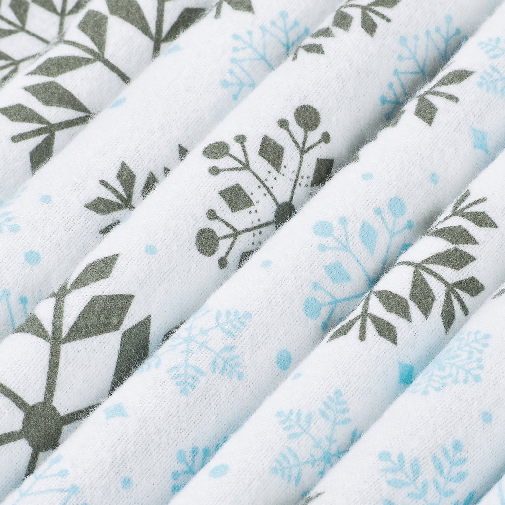 Close-up of folded white fabric with a repeating botanical and snowflake-style print in muted gray-green and light blue.