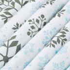 Close-up of folded white fabric with a repeating botanical and snowflake-style print in muted gray-green and light blue.