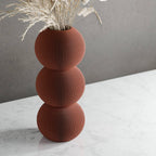 Brown textured vase with dried plants on a white surface and gray background