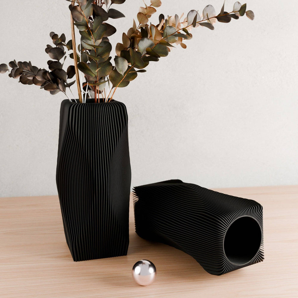 Black ribbed vase with dried plants on a wooden surface