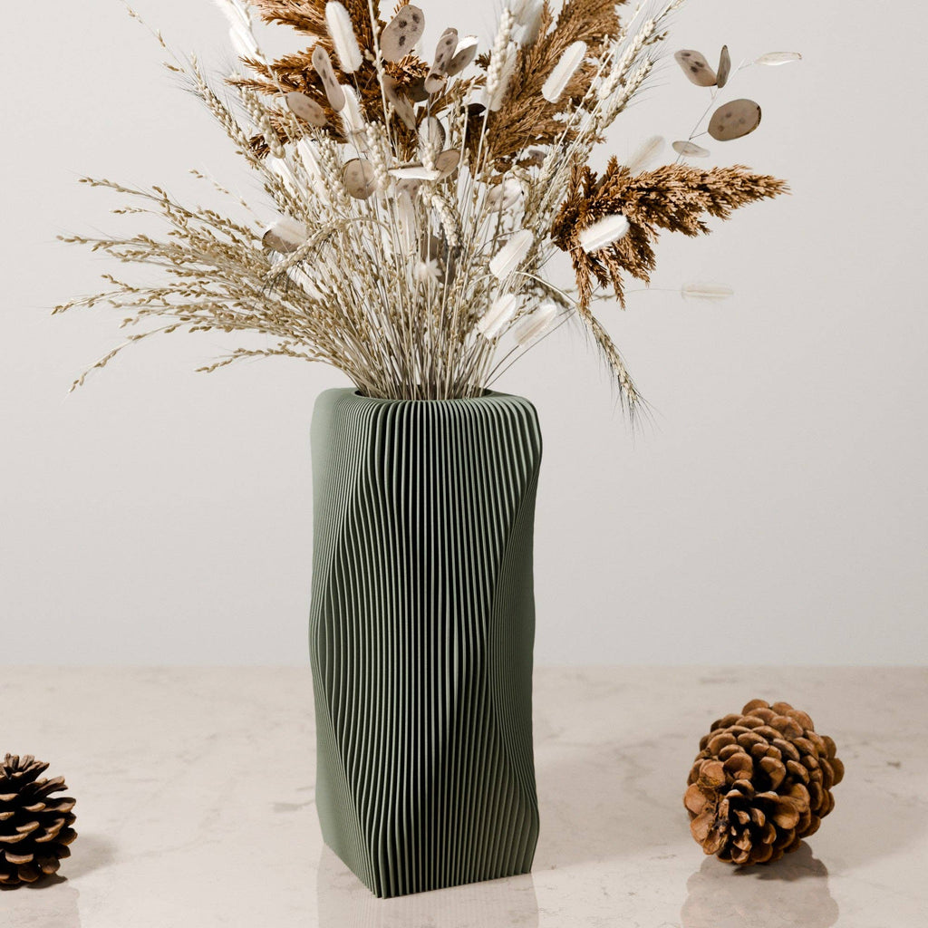 Decorative vase with wavy pattern containing dried plants on a light surface.