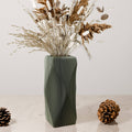 Decorative vase with wavy pattern containing dried plants on a light surface.