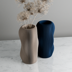Two textured vases, one beige and one blue, on a marble surface with a gray background.