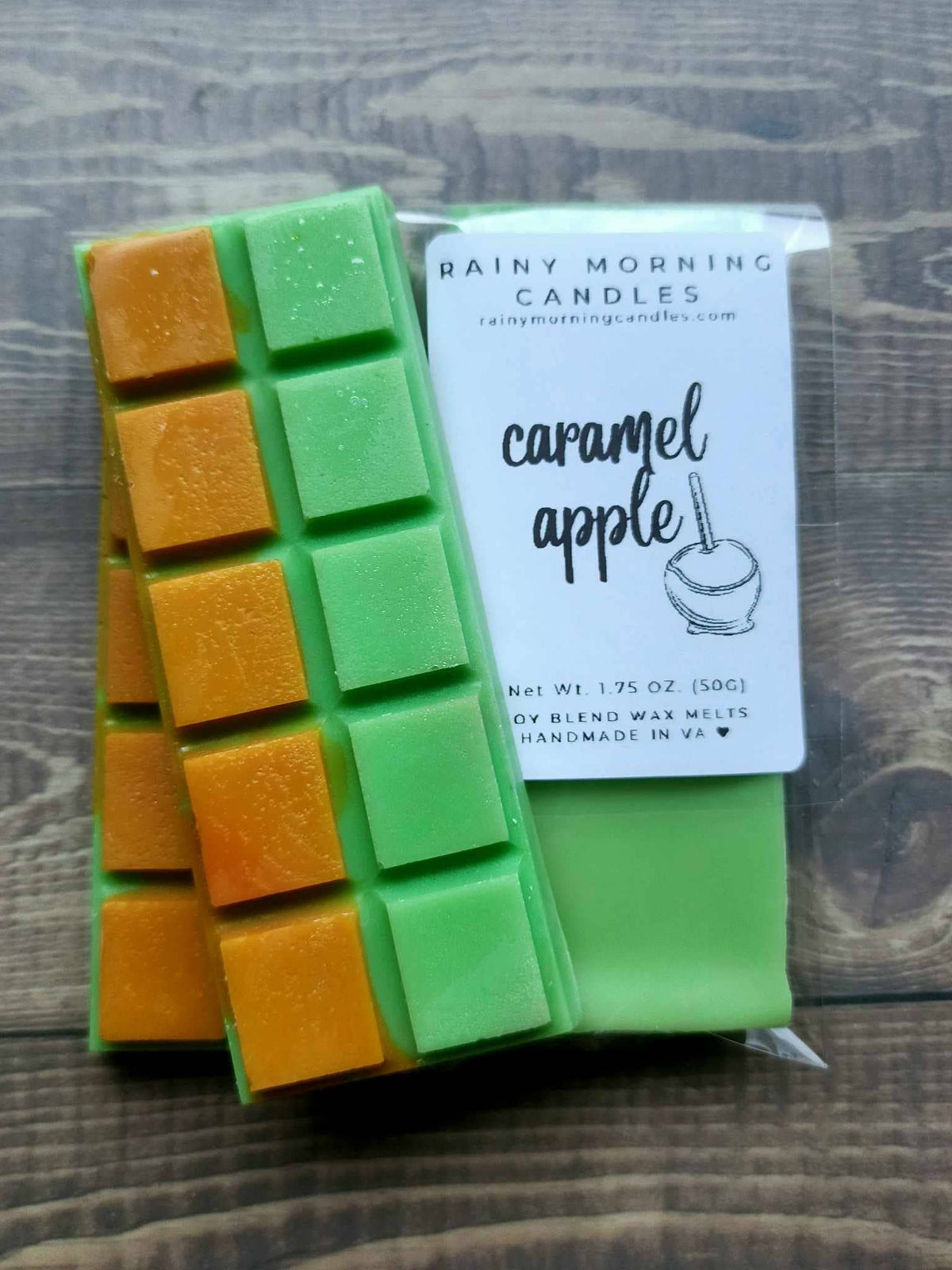 Caramel Apple soy wax melt snap bar in clear packaging with the Rainy Morning Candles label; green wax with caramel-orange squares on a wooden surface.