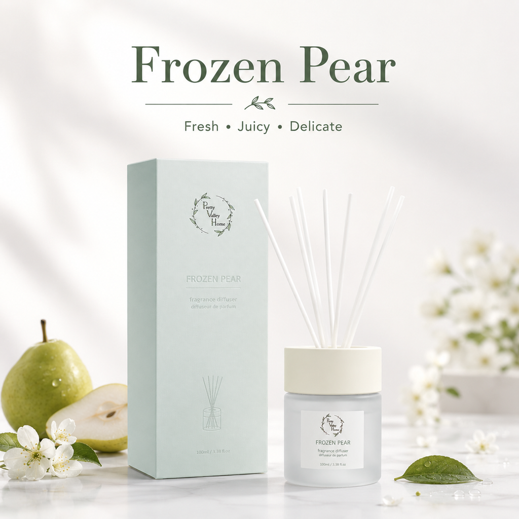A reed diffuser set labeled Frozen Pear, shown with its pale mint box, frosted glass bottle, white cap, and white reeds, styled on a light surface with a green pear, white blossoms, and soft shadows. Large text at the top reads Frozen Pear with the tagline Fresh Juicy Delicate.