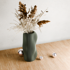 Green textured vase with dried plants on a wooden surface