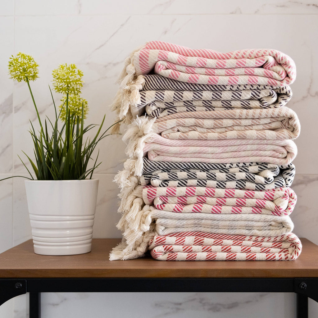 Stack of patterned blankets on a table with a plant in the background