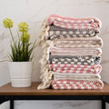 Stack of patterned blankets on a table with a plant in the background
