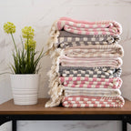 Stack of patterned blankets on a table with a plant in the background