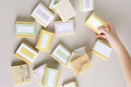 Hand picking a soap bar from a collection of neatly arranged soap bars on a light surface.
