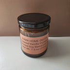 An amber glass jar candle with a black lid and a peach-colored label reading 'SOMA HOME DECOR Toasted Vanilla Pumpkin Scented Soy Blend Candle Net Wt. 7.