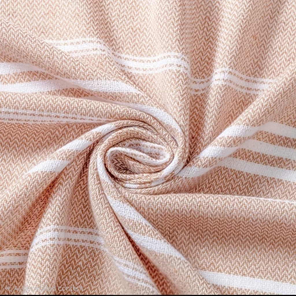 A close-up of a woven textile with a soft peach-beige and white herringbone pattern, arranged in a spiral drape to show the fabric texture and color.