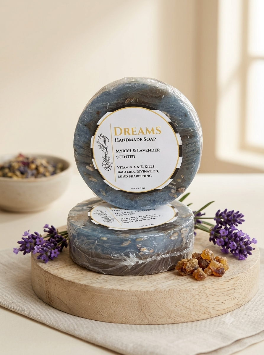 Two round bars of Dreams Handmade Soap stacked on a wooden display block, with lavender sprigs and dried botanicals around them. The top bar has a visible label reading 'Dreams Handmade Soap Myrrh & Lavender Scented'.
