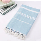 Folded light blue Turkish beach towel with white stripes and tassels beside a stack of books