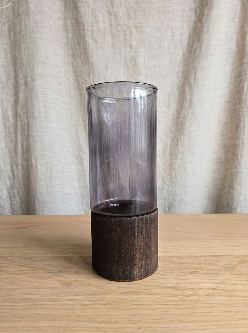 Smoky smooth glass vase on a dark wooden base, studio shot