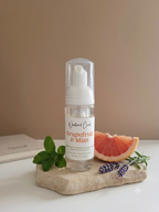 A clear pump bottle labeled 'Nordic Co. Grapefruit & Mint' stands on a stone slab with a grapefruit slice, mint leaves, and lavender sprigs against a warm beige background.