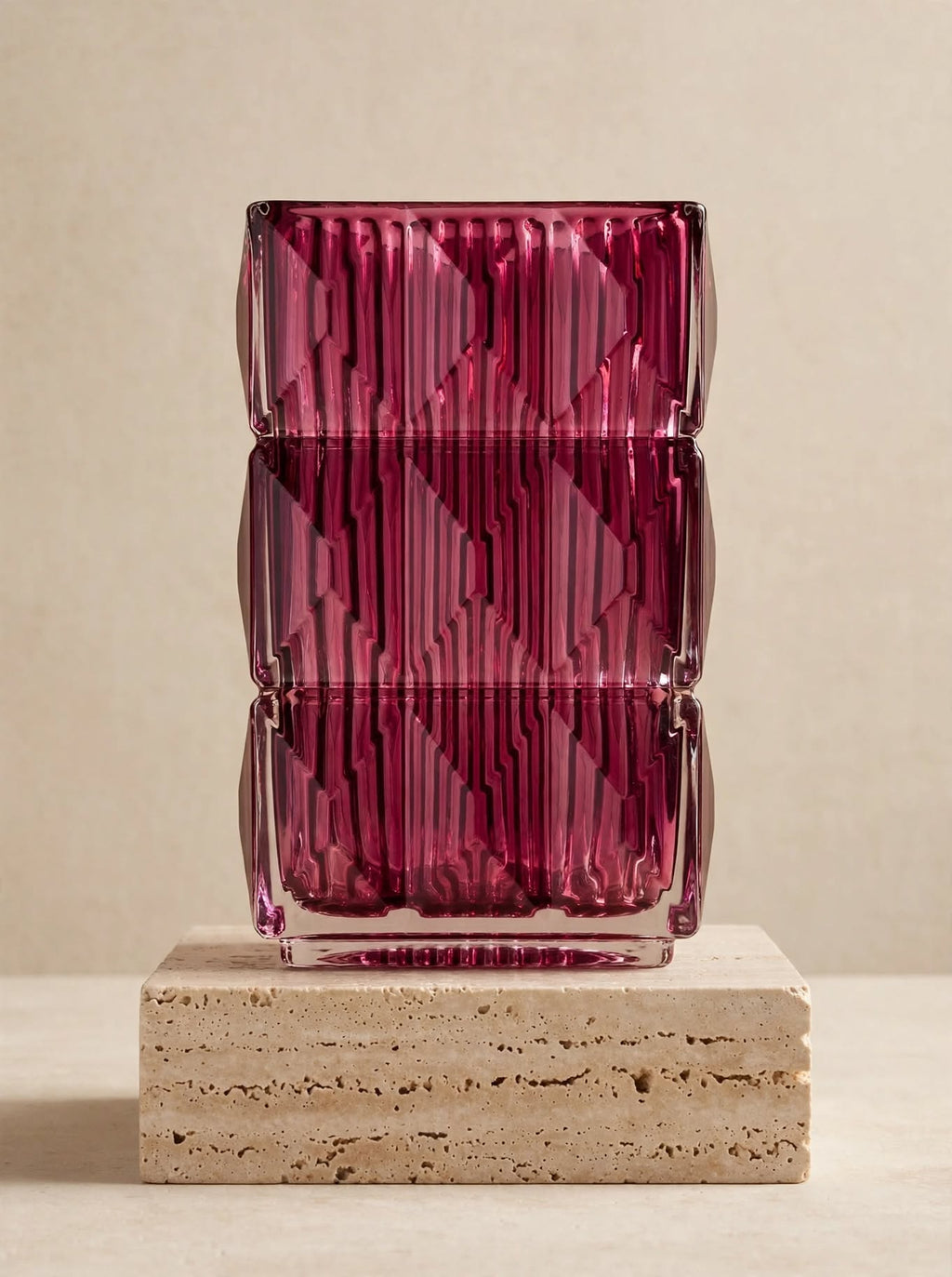 Magenta square glass vase with geometric ice-crackle texture displayed on a travertine pedestal