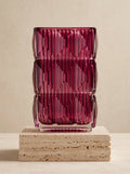 Magenta square glass vase with geometric ice-crackle texture displayed on a travertine pedestal