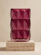 Magenta square glass vase with geometric ice-crackle texture displayed on a travertine pedestal
