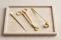 Gold candle care set: wick trimmer, snuffer and dipper arranged on a travertine tray