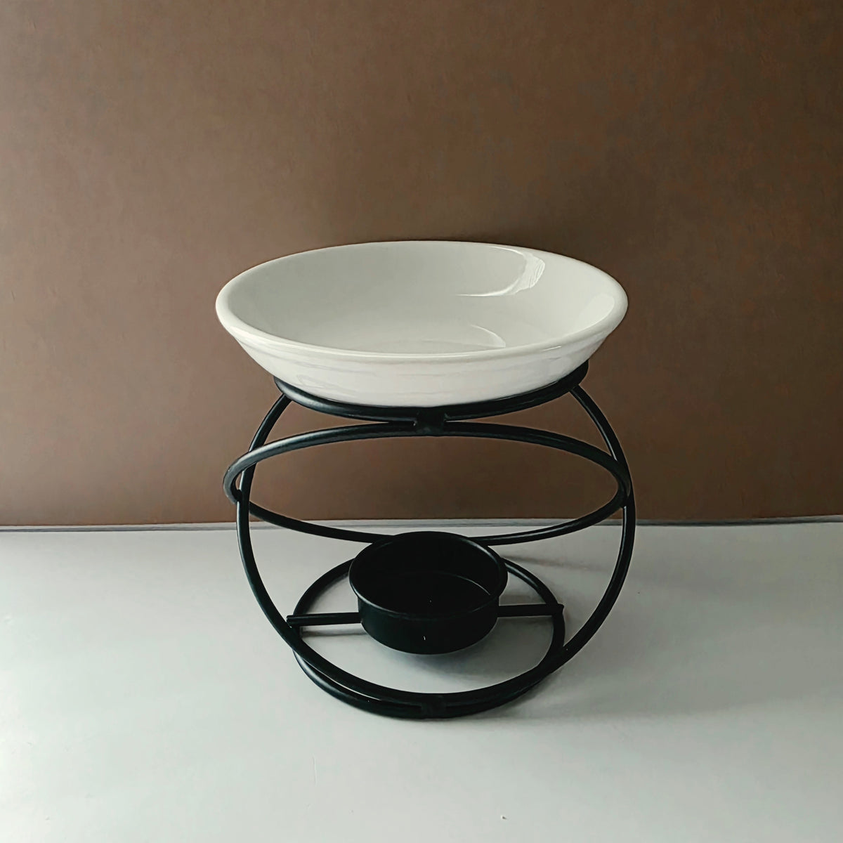 A white ceramic bowl elevated on a black metal stand with a circular base, photographed against a plain brown wall and white surface.