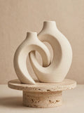 Matte white interlocking ceramic donut vases on a travertine pedestal