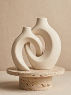 Matte white interlocking ceramic donut vases on a travertine pedestal