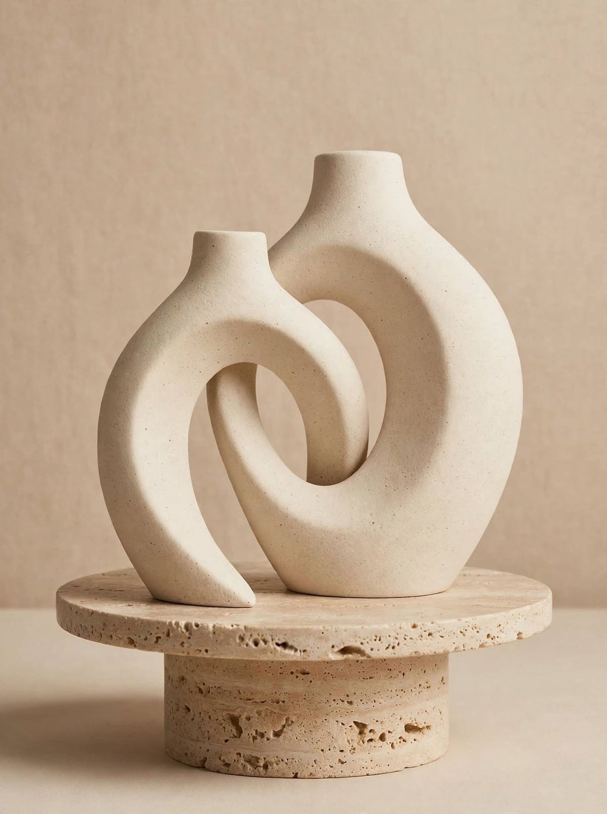Matte white interlocking ceramic donut vases on a travertine pedestal