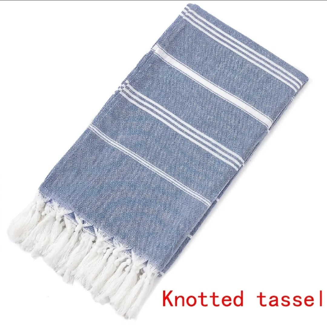 Folded dark blue Turkish beach towel with white stripes and knotted tassels on white background