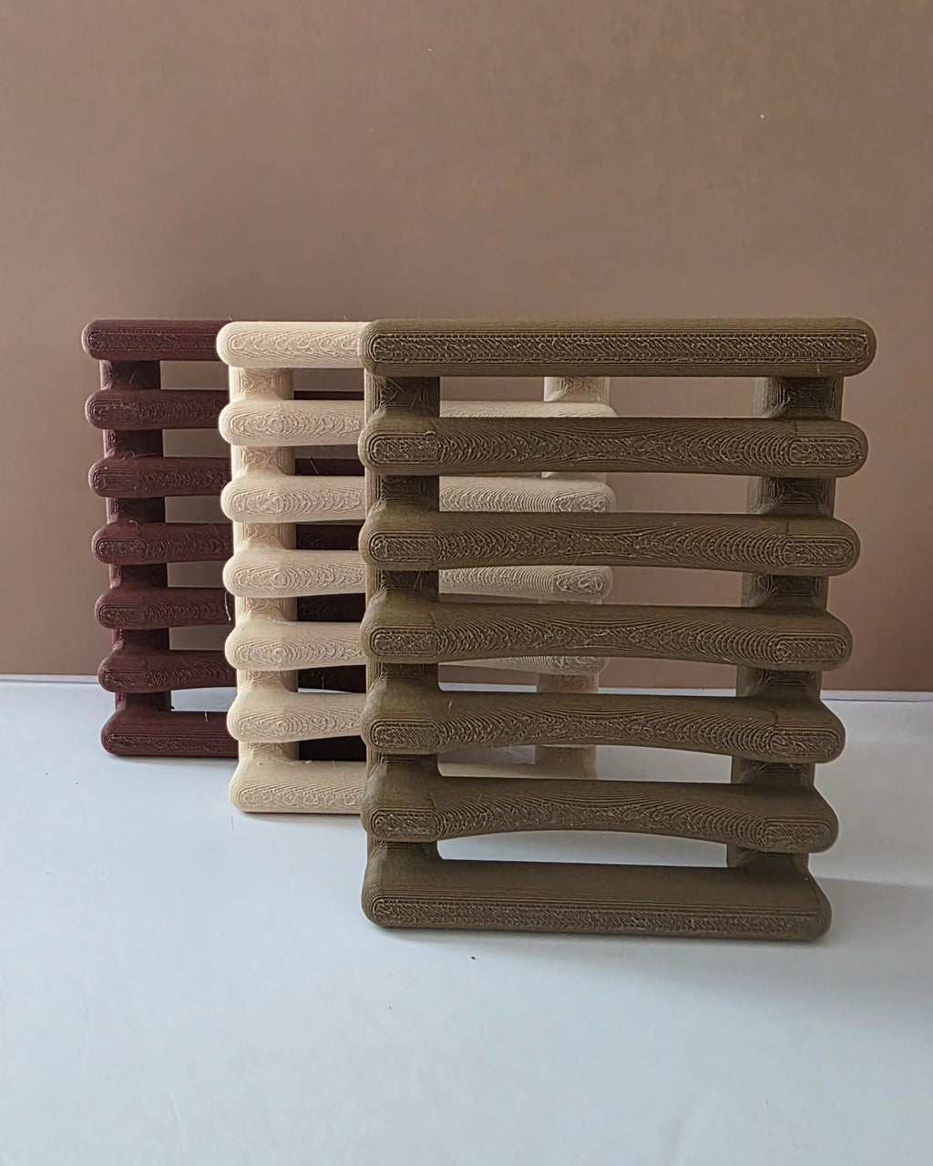 Three slatted rectangular pet stools or cat towers in brown, beige, and burgundy, arranged on a white surface against a plain tan background.