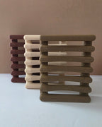 Three slatted rectangular pet stools or cat towers in brown, beige, and burgundy, arranged on a white surface against a plain tan background.