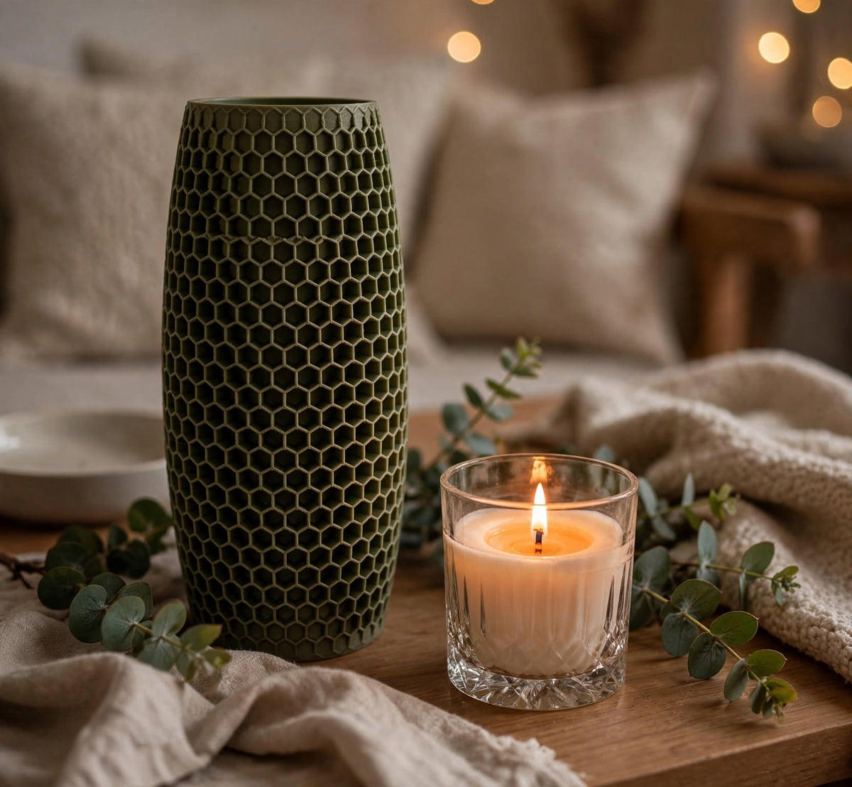 Muted green honeycomb-textured vase styled on a wooden table next to a lit soy candle and eucalyptus sprigs