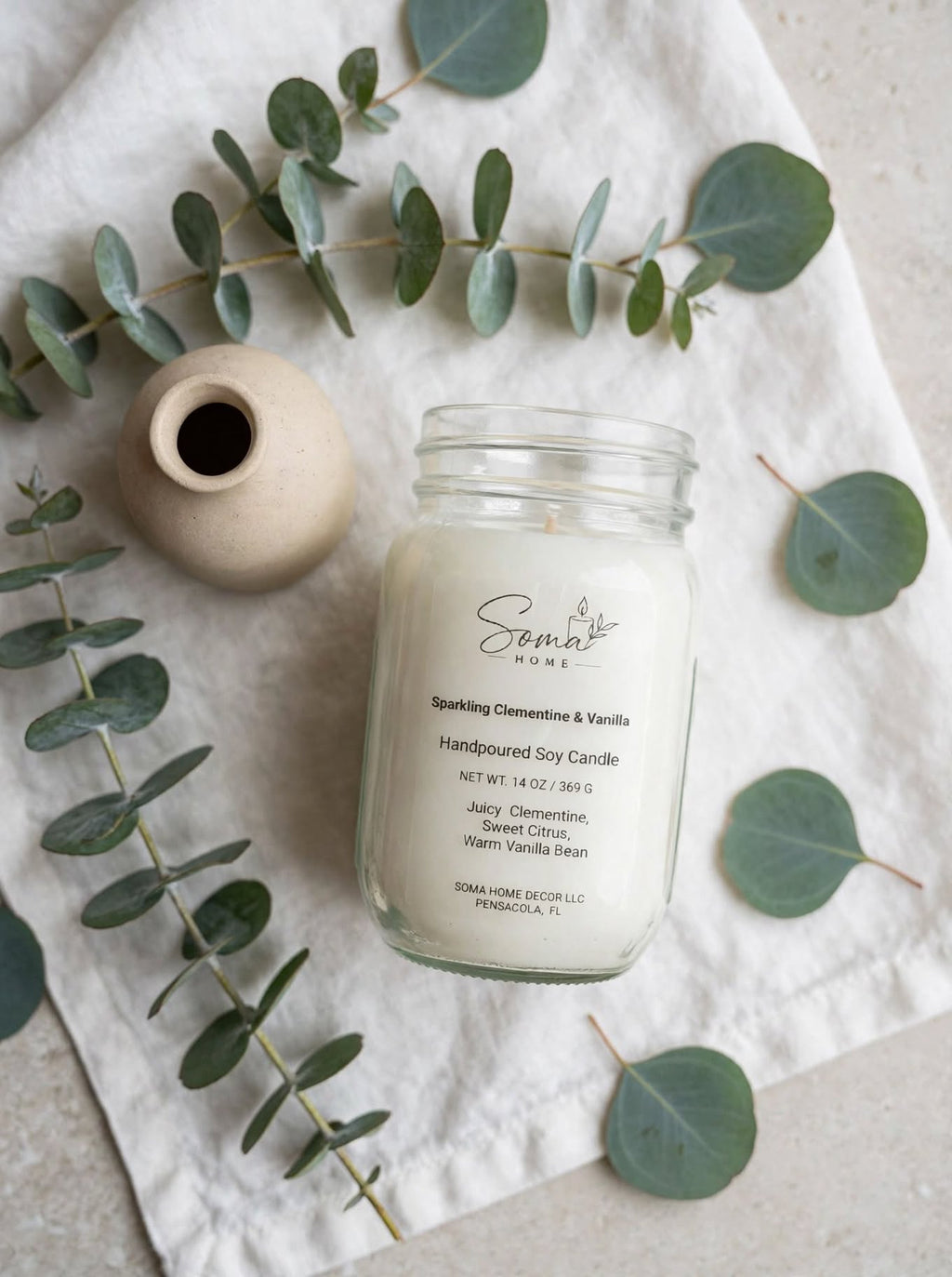 Sparkling Clementine and Vanilla 14 oz soy candle in a mason jar styled with eucalyptus on white linen