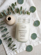 Sparkling Clementine and Vanilla 14 oz soy candle in a mason jar styled with eucalyptus on white linen