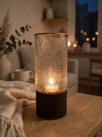 Clear bark-textured glass vase glowing with a lit candle inside at night