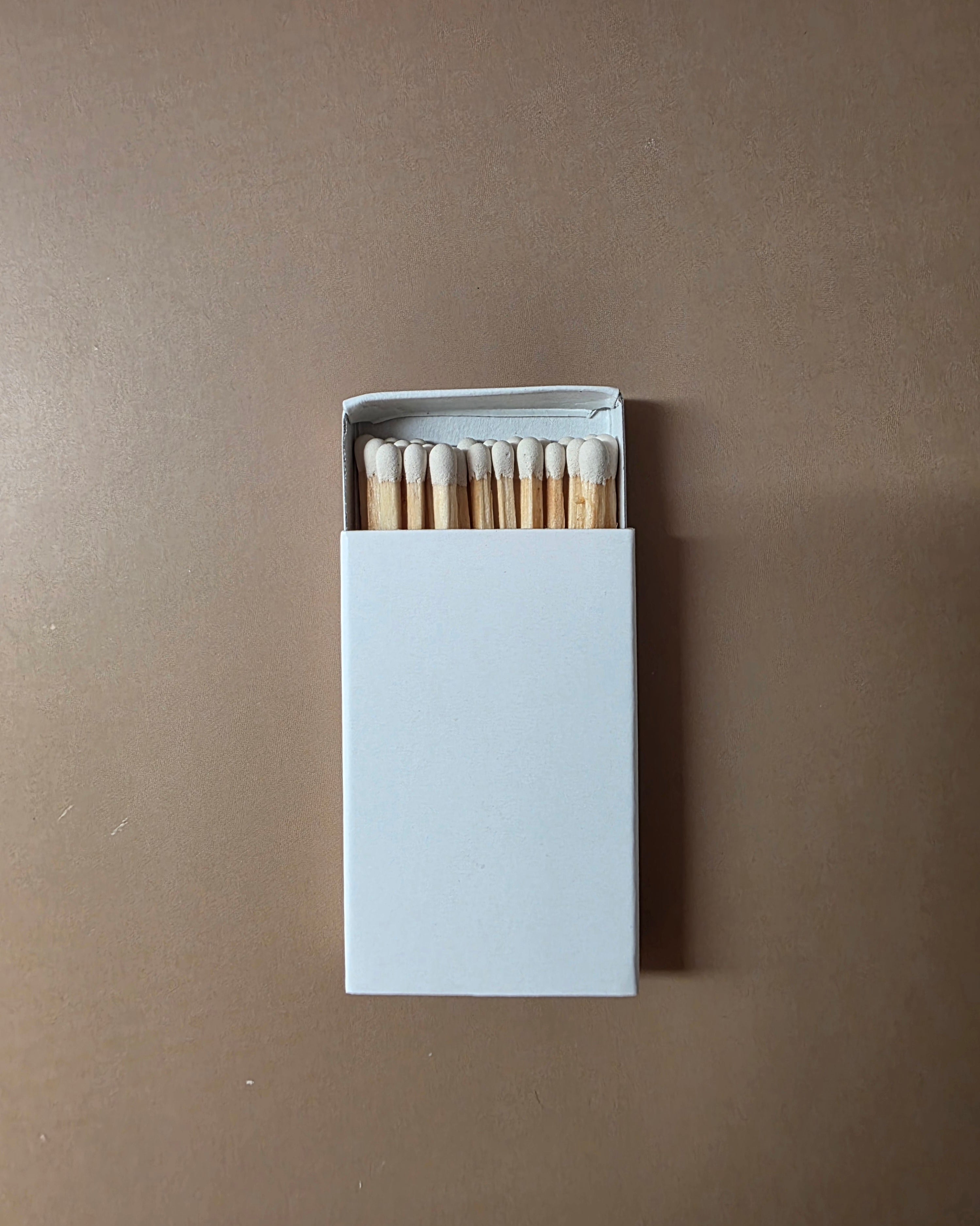 An open white matchbox with wooden matches inside, centered on a plain brown background.