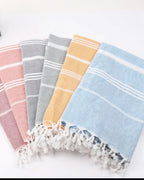 Turkish beach towels in coral pink, gray, mustard yellow and light blue with white tassels, folded on white background