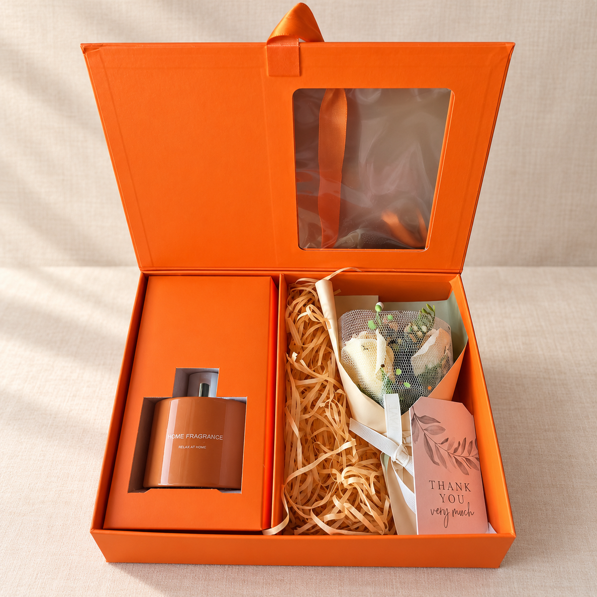 Reed diffuser gift set with bouquet: open orange gift box with home fragrance diffuser and white rose bouquet on shredded kraft paper with a Thank You tag
