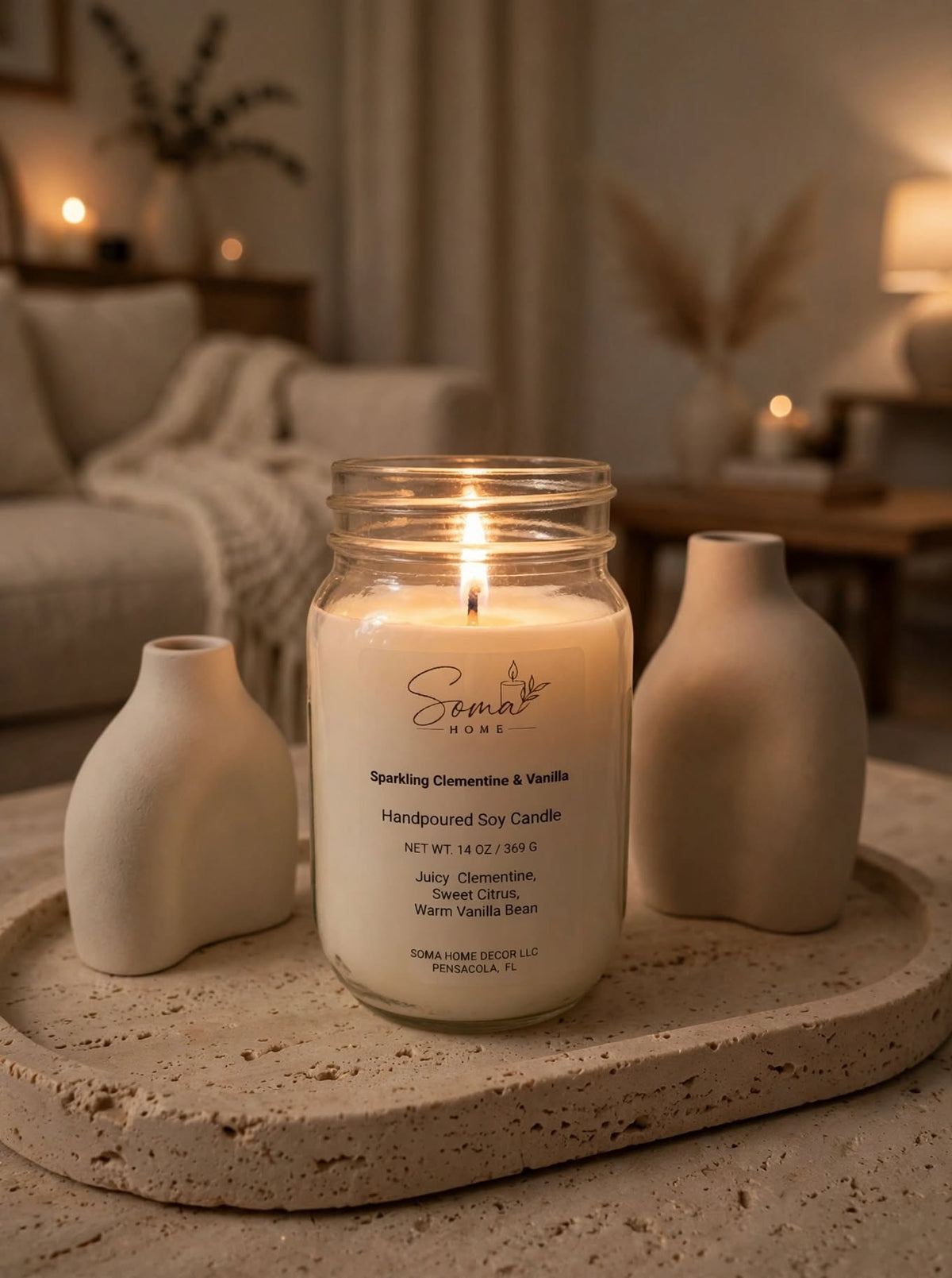 Lit Sparkling Clementine and Vanilla soy candle in a 14 oz mason jar on a stone tray with beige ceramic vases