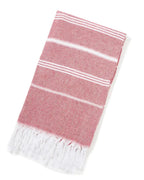 Folded red Turkish beach towel with white stripes and white tassels on white background