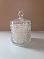 A clear cut-glass jar with a matching pointed lid, containing a white candle, set against a plain beige and white background.