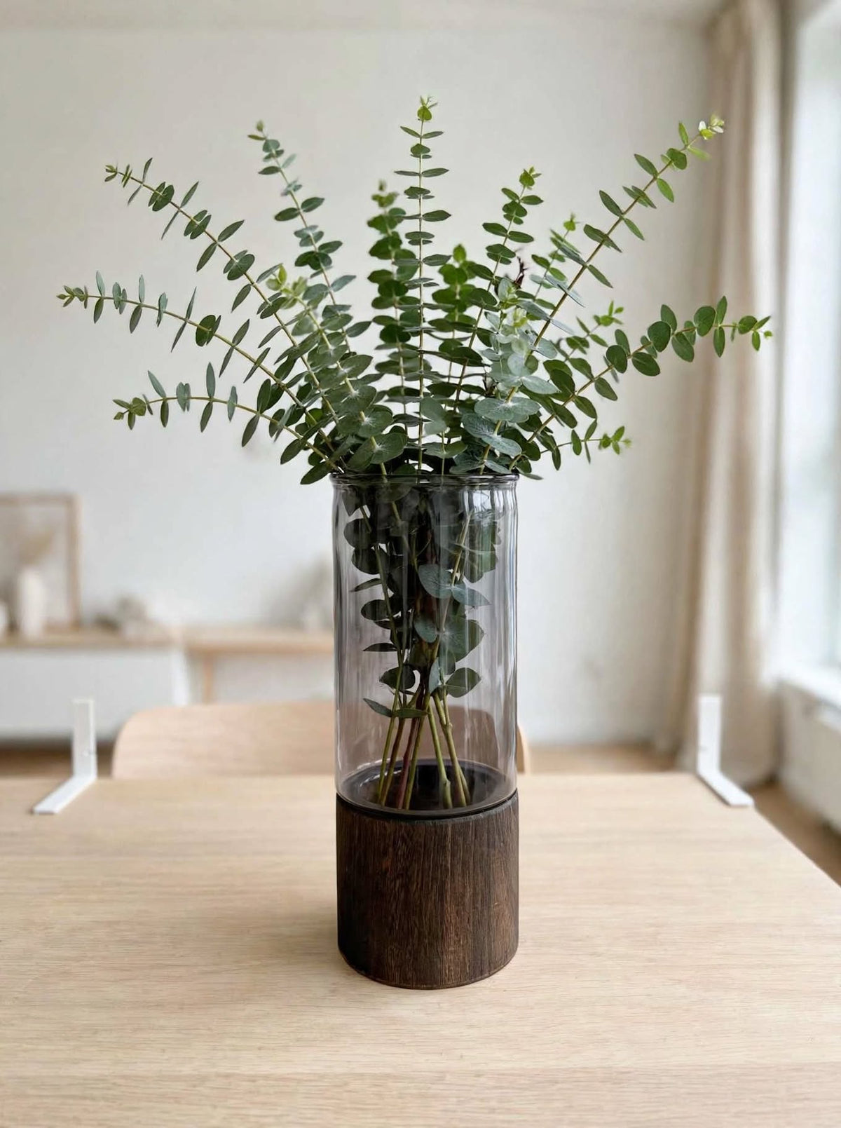 Smoky smooth glass vase on wooden base styled with eucalyptus