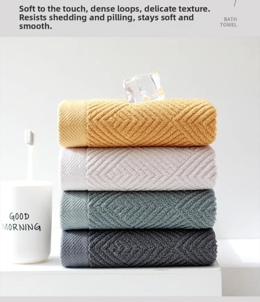 Stack of four folded cotton hand towels in mustard yellow, white, sage green and dark gray with jacquard rhombus weave